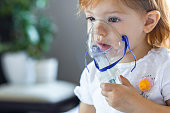 Cute toddler girl are sitting and holds a nebulizer mask leaning against the face, concept airway treatment