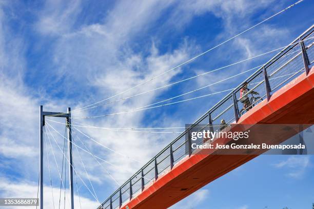 red bridge against blue sky on clear morning. pedestrians and cyclists running on it. alcorcón, madrid, spain. - suspension bridge stock pictures, royalty-free photos & images