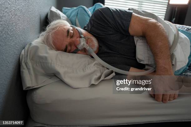 hombre maduro que duerme con una máquina cpap (presión positiva continua en las vías respiratorias) después de ser diagnosticado con apnea del sueño - nose mask fotografías e imágenes de stock