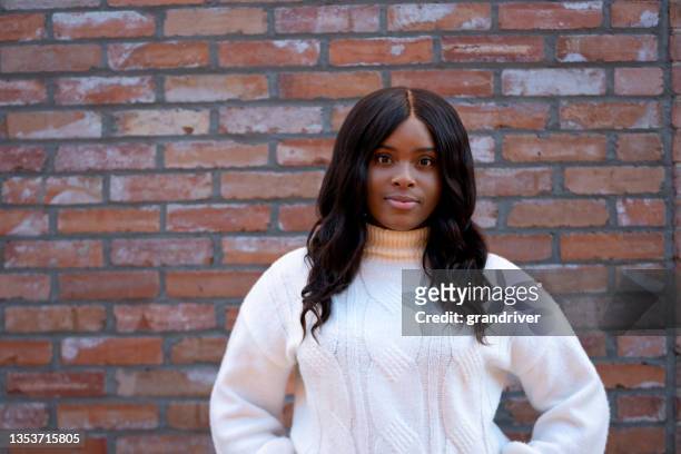 beautiful young african american woman smiling at camera with long straight black hair in front of a brick wall - single brick stock pictures, royalty-free photos & images