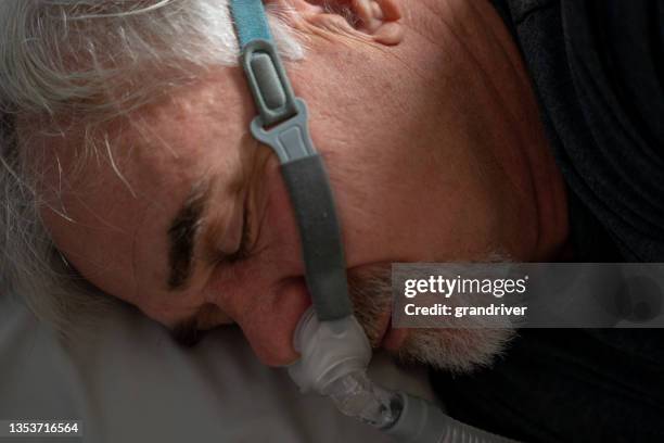 mature man sleeping with a cpap (continuous positive airway pressure) machine after being diagnosed with sleep apnea - bruxism stock pictures, royalty-free photos & images