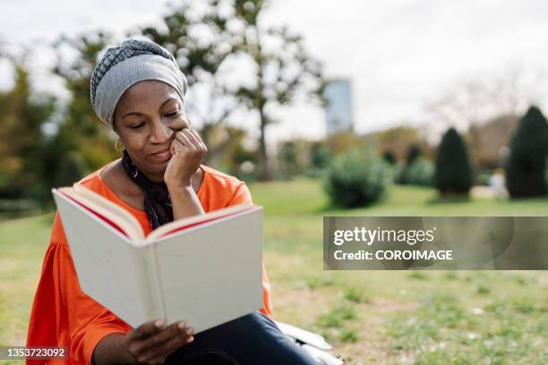 mujer disfrutando de la lectura de un libro sentada en la hierba de un parque. ature concept. - mujer sentada stock-fotos und bilder