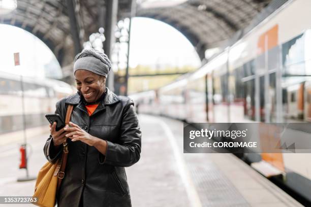 woman smiling while using her smartphone on the platform at the train station. - train platform bildbanksfoton och bilder