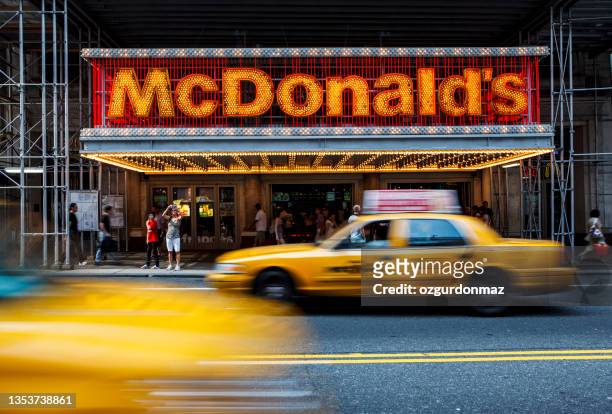 large group of people and yellow taxis passing by at the entrance to mcdonalds fast-food restaurant in midtown manhattan - mcdonald imagens e fotografias de stock