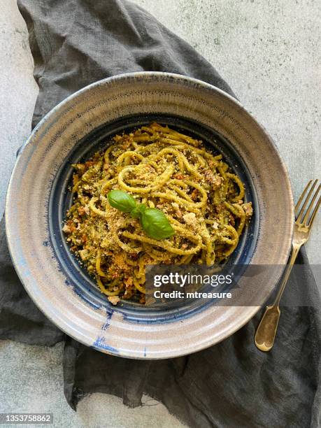 imagen de plato azul y blanco de pesto casero, pasta de espaguetis cubierta con pan rallado y hojas de albahaca, tenedor dorado, muselina gris, vista elevada - pan rallado fotografías e imágenes de stock
