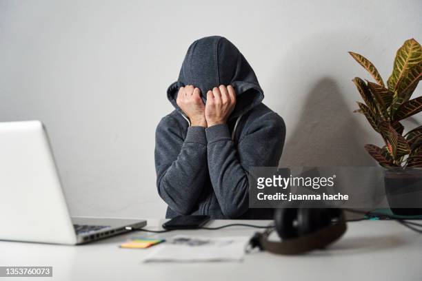 tired man covering his face with a hood while working from home. - head in hands computer stock pictures, royalty-free photos & images