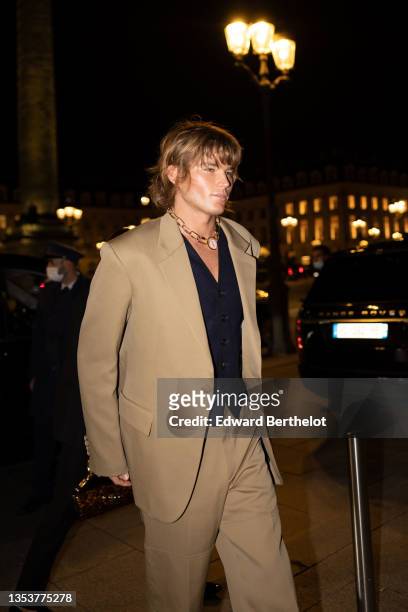 Jordan Barrett wears a large gold chain with diamond pendant necklace from Messika, a black buttoned V-neck blazer, a beige blazer jacket, matching...