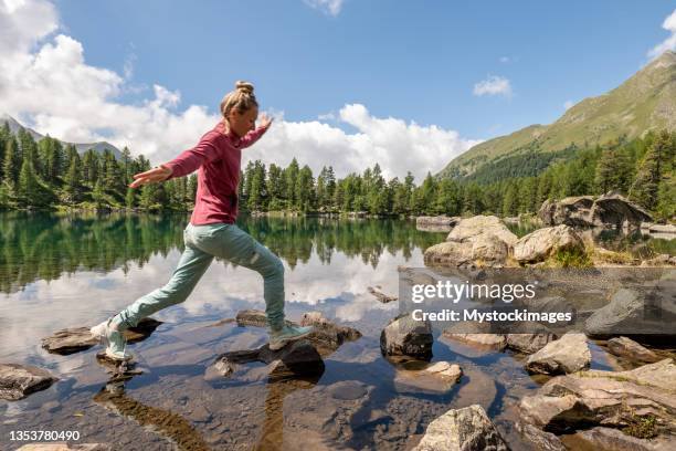 female hiker jumps from rock to rock above alpine lake - agile transformation stock pictures, royalty-free photos & images