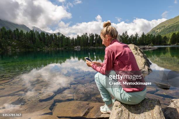 mujer en el teléfono móvil cerca del lago alpino - sunday in the valley fotografías e imágenes de stock