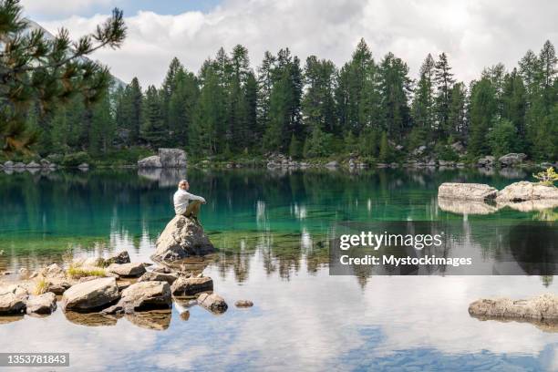 man sits on a rock in a middle of an alpine lake - graubunden canton stock pictures, royalty-free photos & images