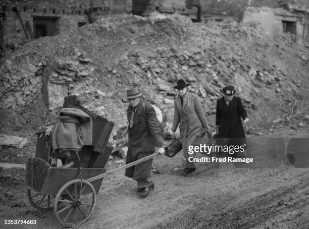 Homeless German civilians carry their bundles of clothes and possessions in suitcases and a hand pushed cart past abandoned bomb damaged buildings in...