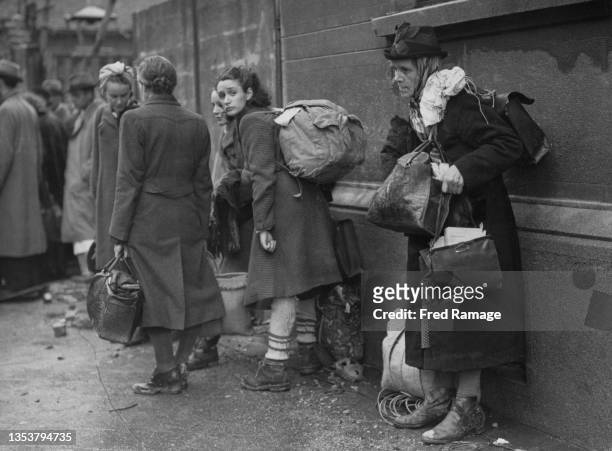 Homeless German civilian refugees carry their bundles of clothes and possessions as they wait to escape the battle for the town by the United States...