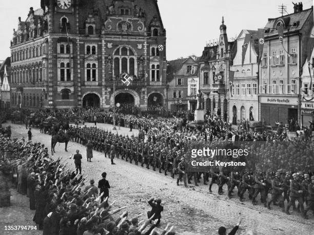 German military bands plays and crowds of people give the Nazi salute as German Wehrmacht troops march through the town square of Friedland in the...