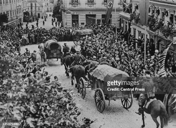 Crowds of people give the Nazi salute as a German Wehrmacht horsedrawn cart supply column passes through the streets of Warnsdorf in the occupied...