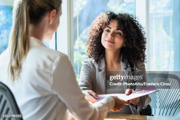 mature woman delivering a document to young woman in office - versicherungsagent stock-fotos und bilder