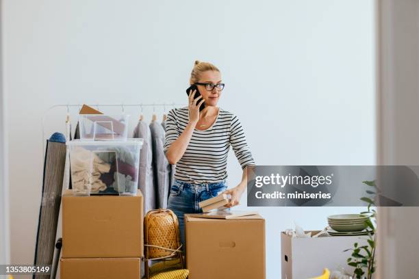 beautiful woman having a call while unpacking boxes in her new apartment - possession stock pictures, royalty-free photos & images