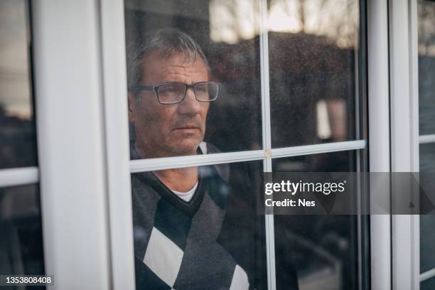 an older depressed man looks out the window - house insulation not posing stock pictures, royalty-free photos & images