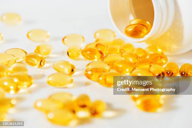 omega 3 fish oil supplement pills spilling from bottle against white marble background - huile de foie de morue photos et images de collection