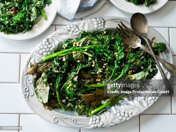 fried broccolini with pine nuts on a vintage serving plate - broccolini stock pictures, royalty-free photos & images