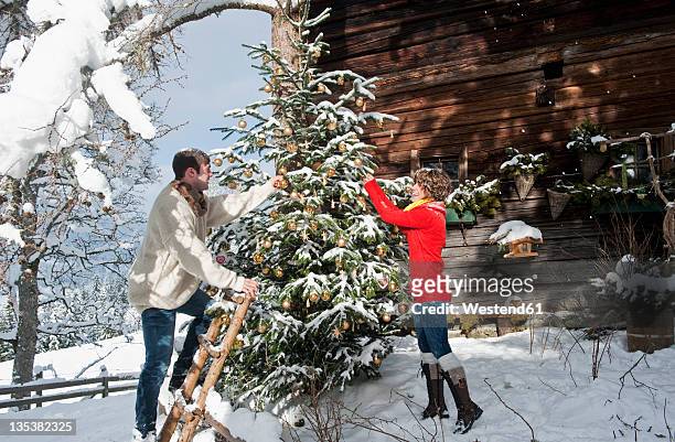 austria, salzburg country, flachau, young man and woman decorating christmas tree in winter - country christmas fotografías e imágenes de stock