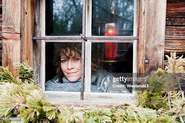 austria, salzburg country, flachau, young woman looking through window in winter - alphütte stock-fotos und bilder