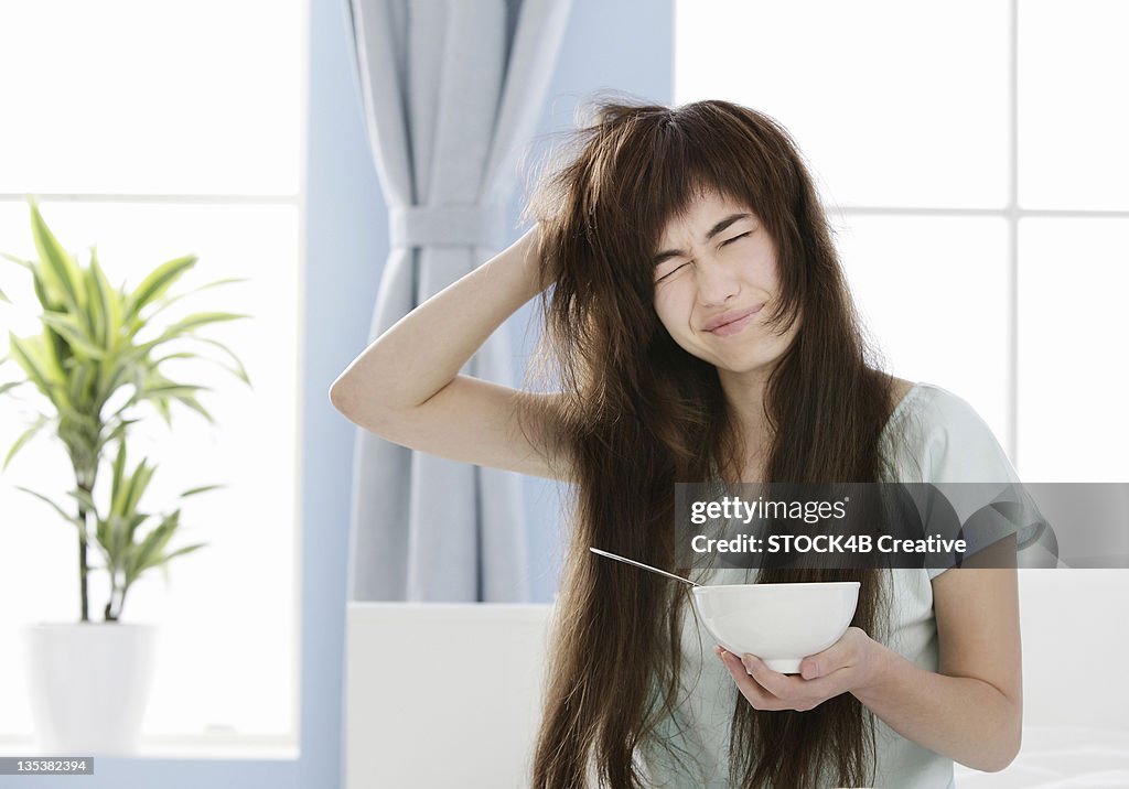 Young woman with muesli bowl disheveling her hair