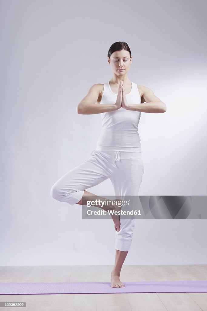 Mid adult woman in tree pose against white background