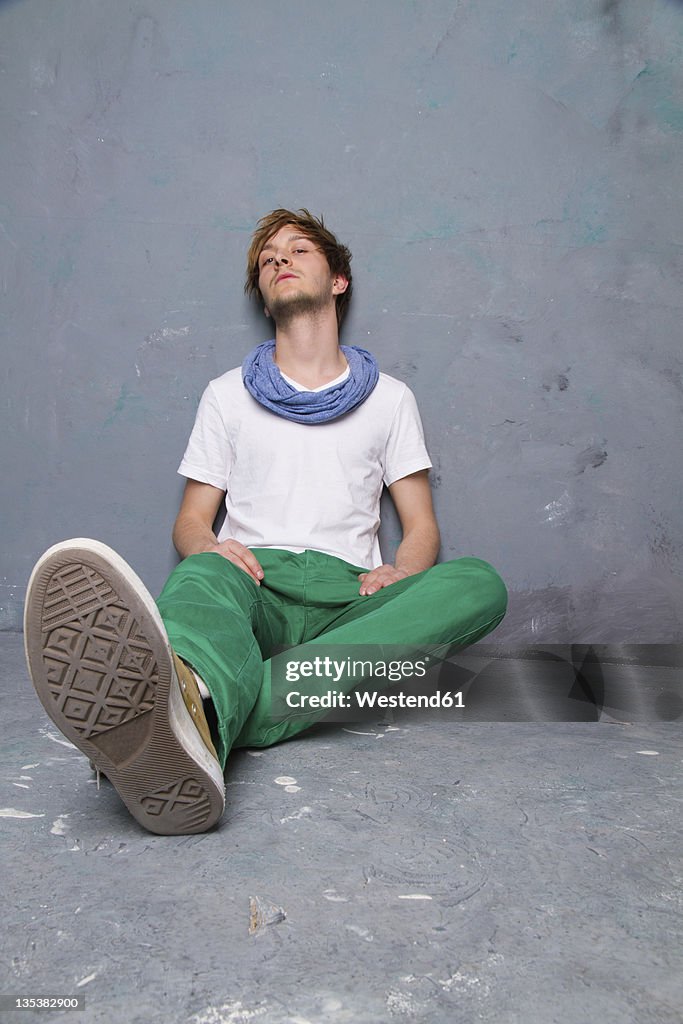 Young man sitting and leaning agaist dirty wall, portrait