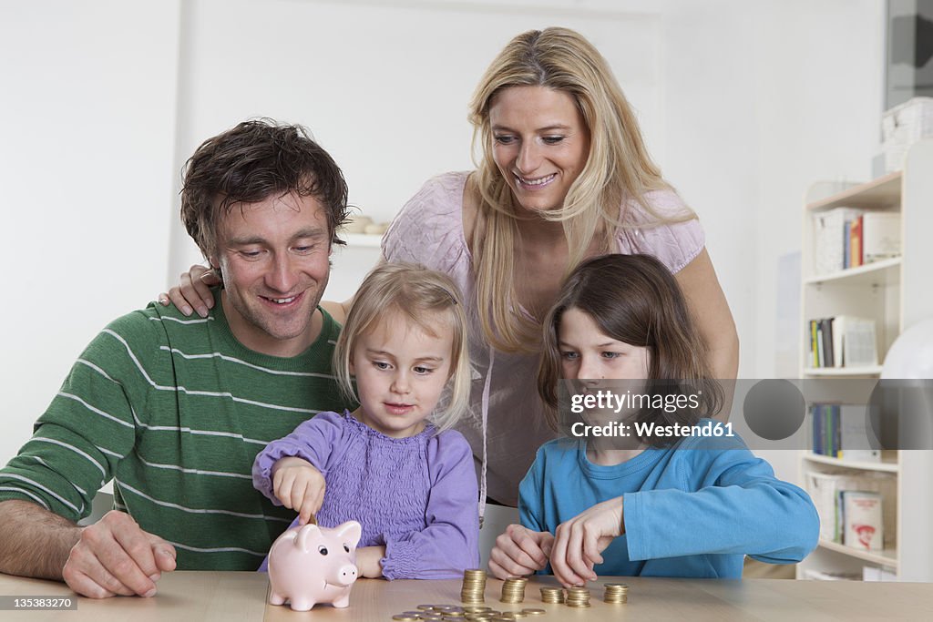 Germany, Bavaria, Munich, Family with coins and piggy bank, smiling