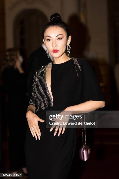 Jessica Wang wears a silver and diamond triangular pendant earrings, a black long dress with ruffled sleeves / asymmetric cut-out neck / embroidered...