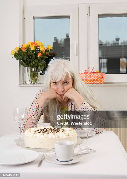 germany, duesseldorf, woman sitting at dining table with cake, flowervase and present, portrait - alleen één oudere vrouw stockfoto's en -beelden