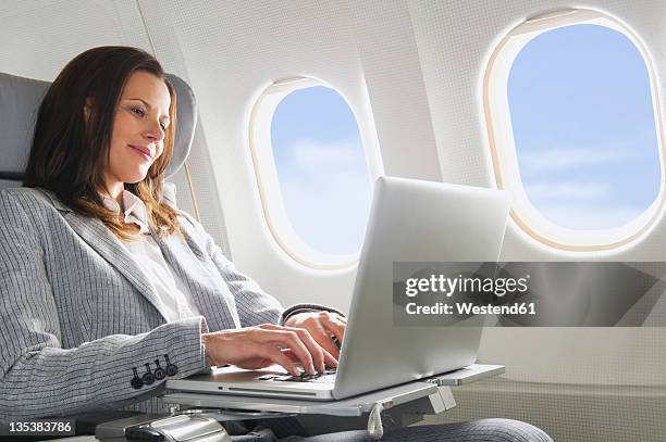 germany, bavaria, munich, mid adult businesswoman using laptop in business class airplane cabin - plane seat stock pictures, royalty-free photos & images