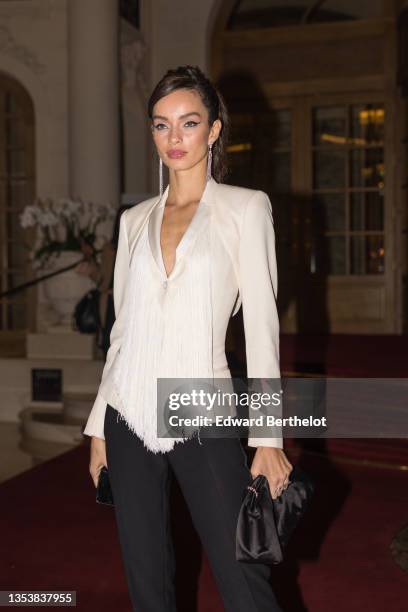 Luma Grothe wears a silver and rhinestones pendant earrings, a white silk V-neck / epaulets blazer jacket with fringed on the chest, high waist black...