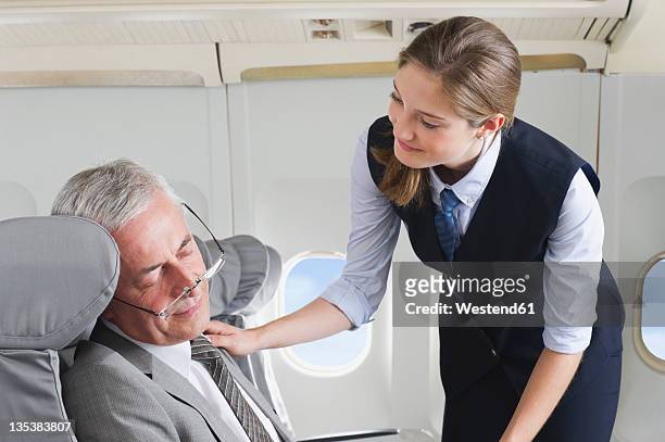germany, bavaria, munich, young stewardess taking care of senior businessman in business class airplane cabin - bent stock pictures, royalty-free photos & images