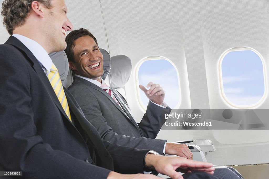 Germany, Bavaria, Munich, Businessmen talking in business class airplane cabin