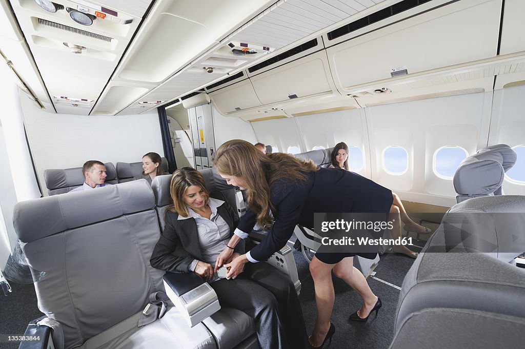 Germany, Bavaria, Munich, Stewardess helping passenger in business class airplane cabin, smiling