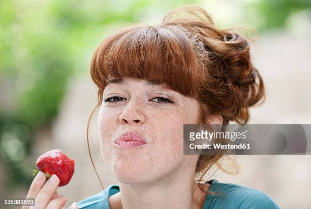 germany, berlin, close up of young woman eating strawberry, smiling, portrait - indulgence photos et images de collection