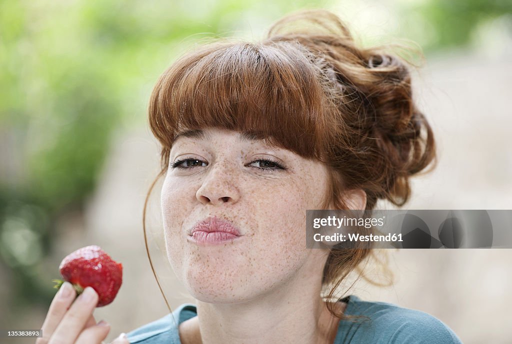 Germany, Berlin, Close up of young woman eating strawberry, smiling, portrait