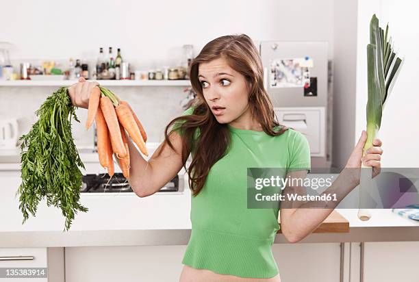 germany, berlin, young woman holding carrots and leek in domestic kitchen - lady cooking confused stock-fotos und bilder