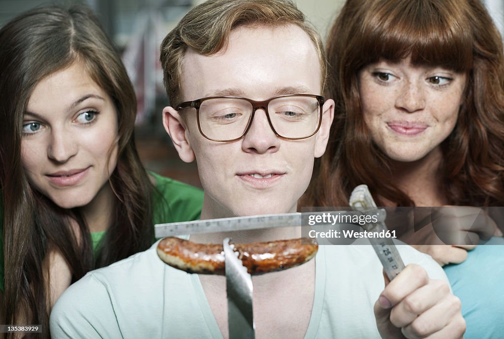 Germany, Berlin, Close up of young man measuring grilled sausage and women beside him, smiling