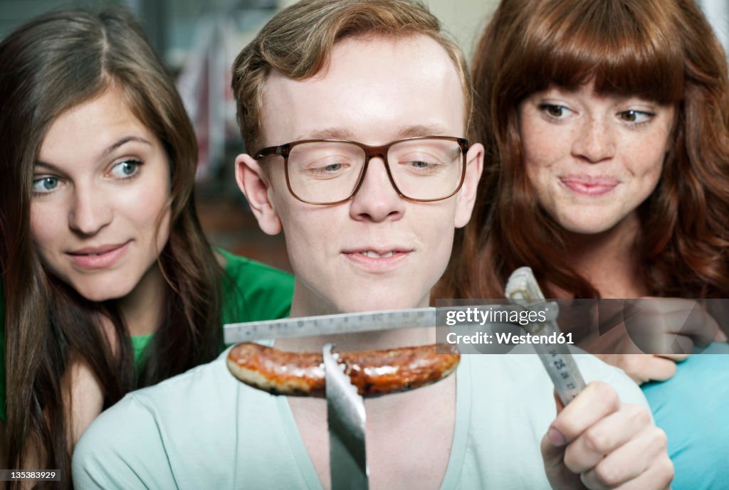 Germany, Berlin, Close up of young man measuring grilled sausage and women beside him, smiling