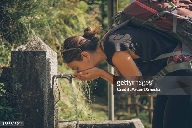 wanderfrau trinkt bergwasser aus dem wasserhahn - süßwasser stock-fotos und bilder
