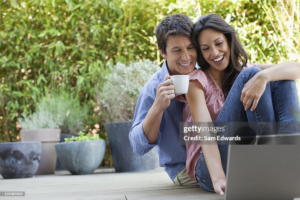Couple relaxing on patio with laptop and coffee