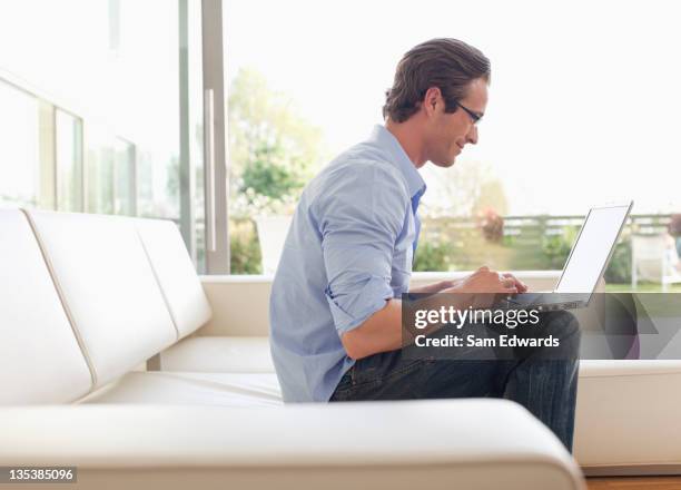 man sitting on sofa using laptop - samuser stock pictures, royalty-free photos & images