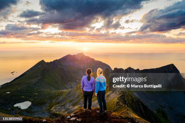 two women admiring the sunset from the top of a mountain in norway - bergen norway stock-fotos und bilder