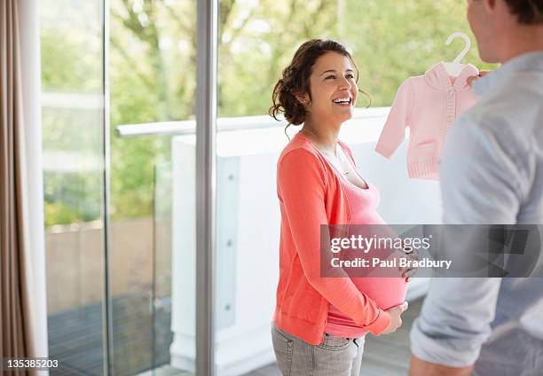 father showing baby clothes to pregnant wife - pregnant belly stock pictures, royalty-free photos & images