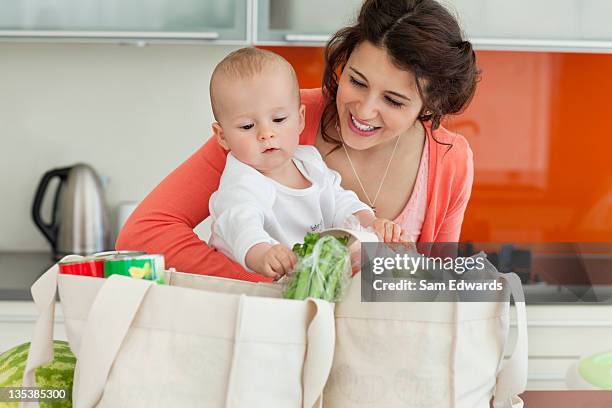 mother holding baby and unloading groceries - baby bag bildbanksfoton och bilder