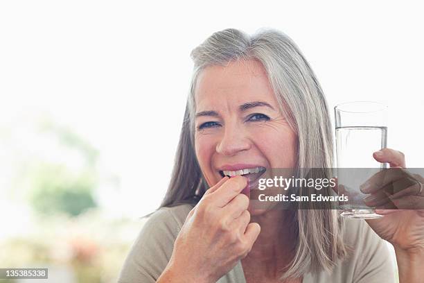 mujer agarrando vaso de agua de tomar píldora - nutritional supplement fotograf�ías e imágenes de stock
