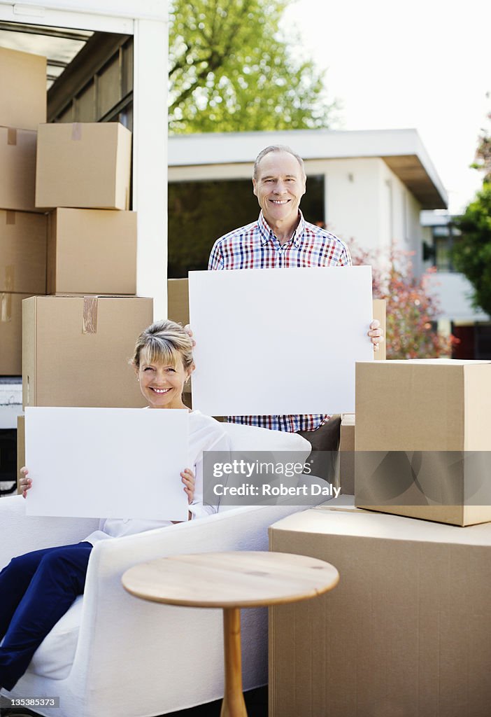 Couple sitting with moving boxes holding blank cards