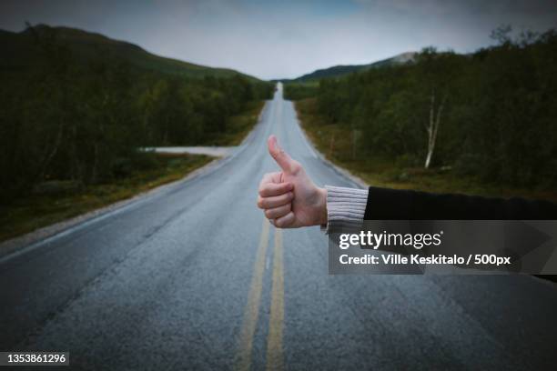 cropped hand of man gesturing hitching sign against sky and road,lappi,finland - hitchhiking 個照片及圖片檔